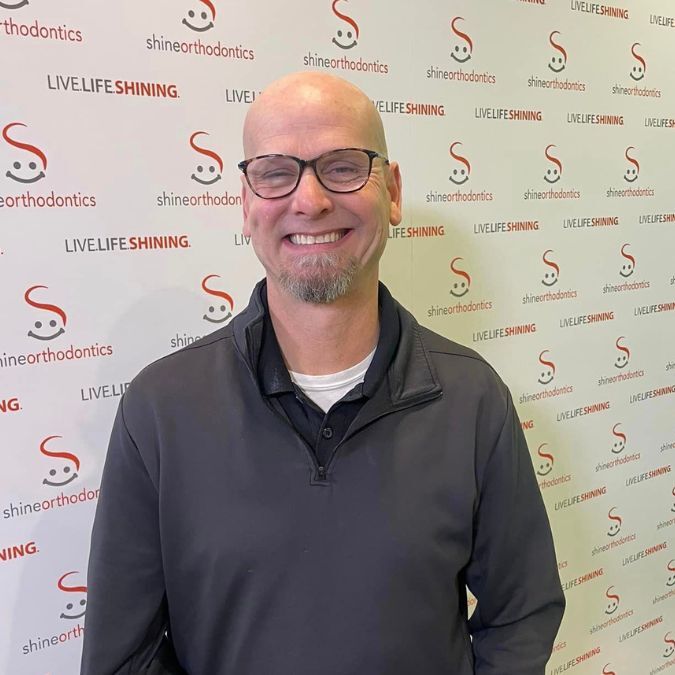 Man smiling in front of Shine Orthodontics backdrop